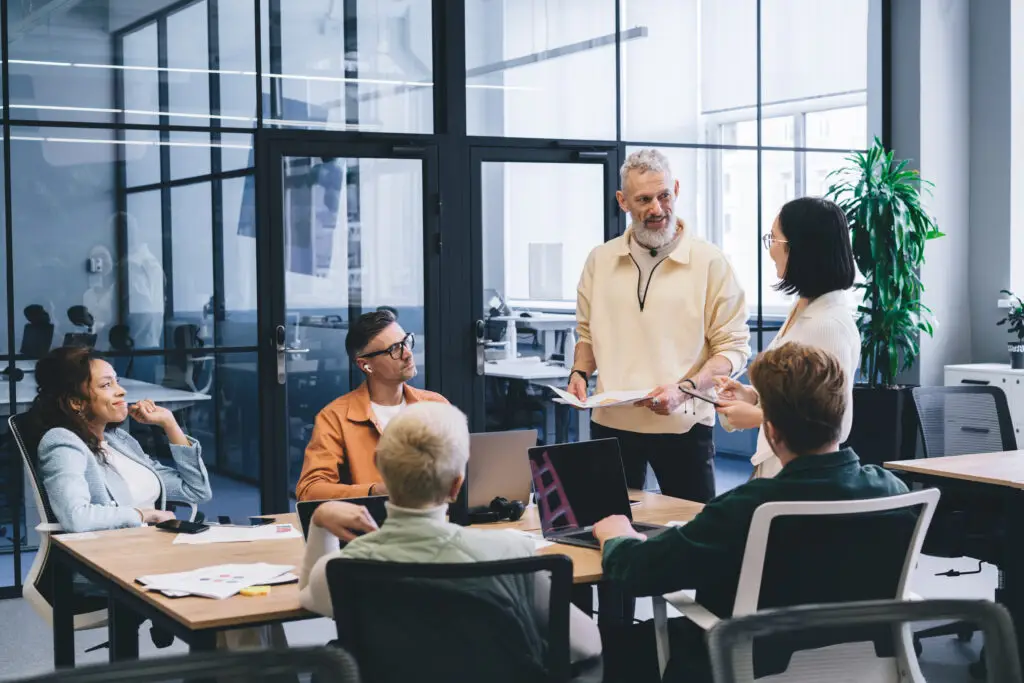 Concentrated multiracial coworkers in casual clothes gathering at table with laptops and documents while brainstorming on ideas for new project together