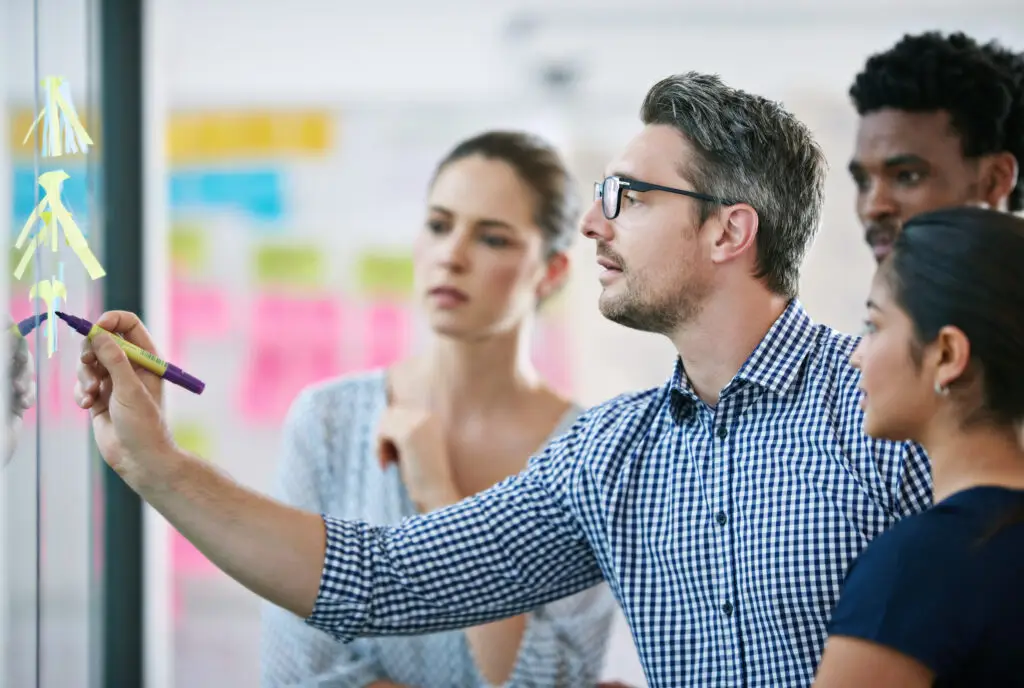 Leader, brainstorming and team design a creative idea in collaboration together in a meeting and planning a strategy. Management, teamwork and group of employees writing vision for a startup company