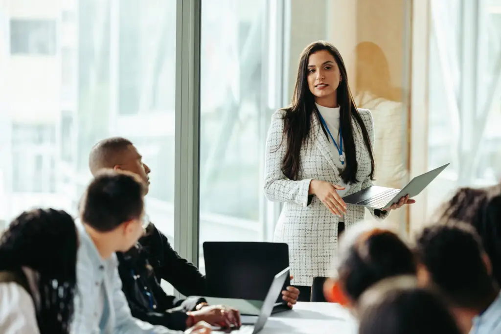 Female business owner confidently presents during a board meeting, showcasing strategies to a diverse team in a modern office environment.